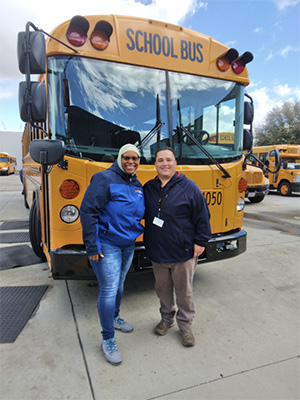 Two staff people in front of a school bus