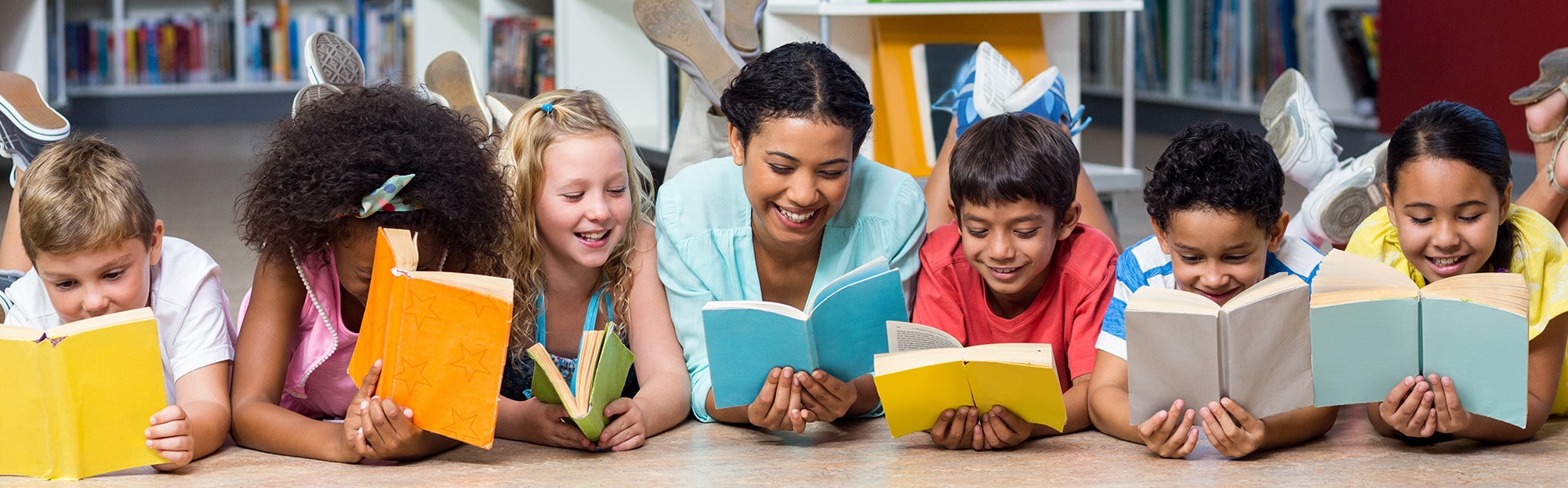 teacher and elementary students reading books on the floor