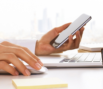 someone holding a phone and using a mouse to work on a computer