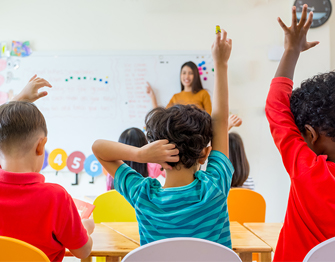 the back of students in a classroom with their hands raised