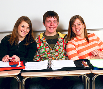 three students sitting in their desks smiling